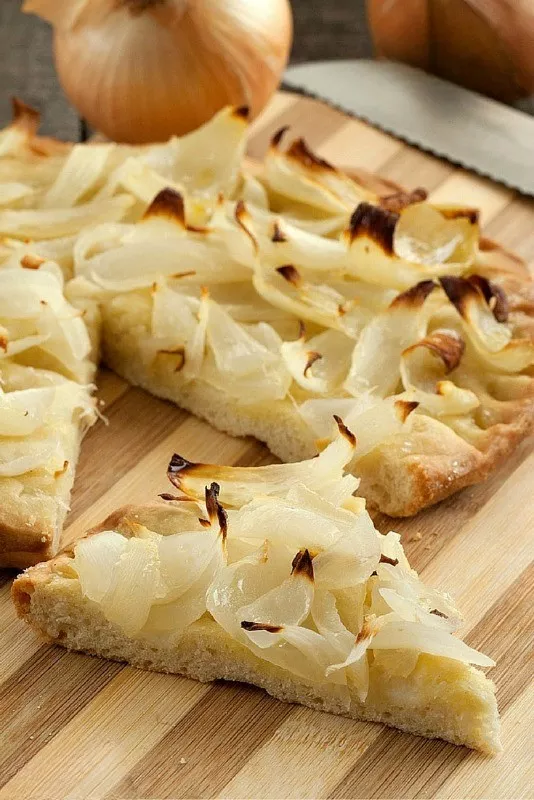 Baked Onion Schiacciata sliced on a wooden board with golden onions on top.