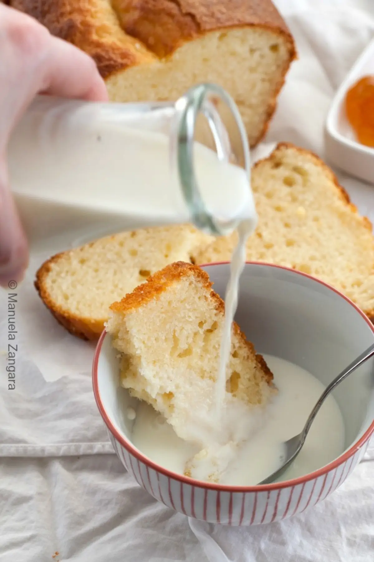 Milk being poured over a slice of yogurt plumcake in a bowl.