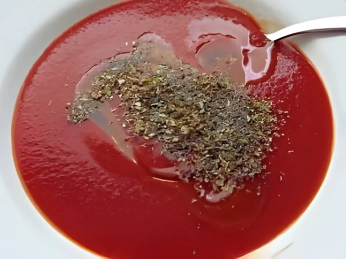 Tomato purée mixed with herbs and olive oil in a white bowl.