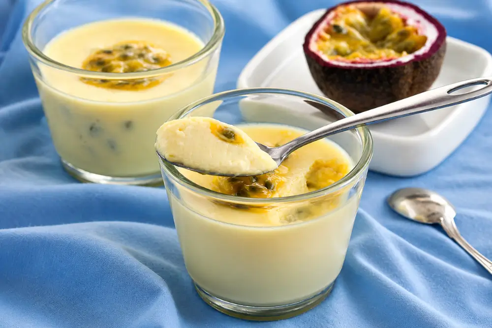 Spoon lifting a silky chilled posset with passion fruit topping from a glass dessert cup.