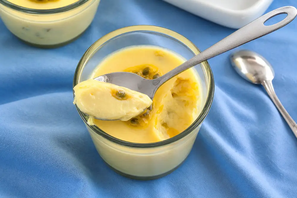 Spoon lifting a creamy passion fruit dessert from a glass ramekin.