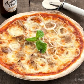 Close-up of a baked tuna and onion pizza with melted cheese and basil.