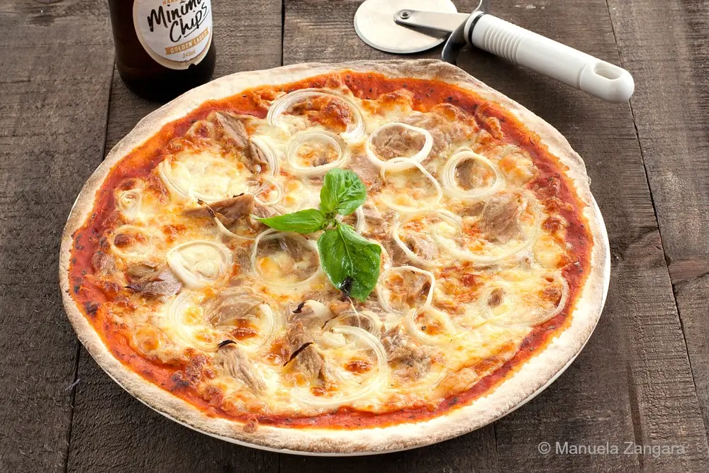 Close-up of a baked tuna and onion pizza with melted cheese and basil.