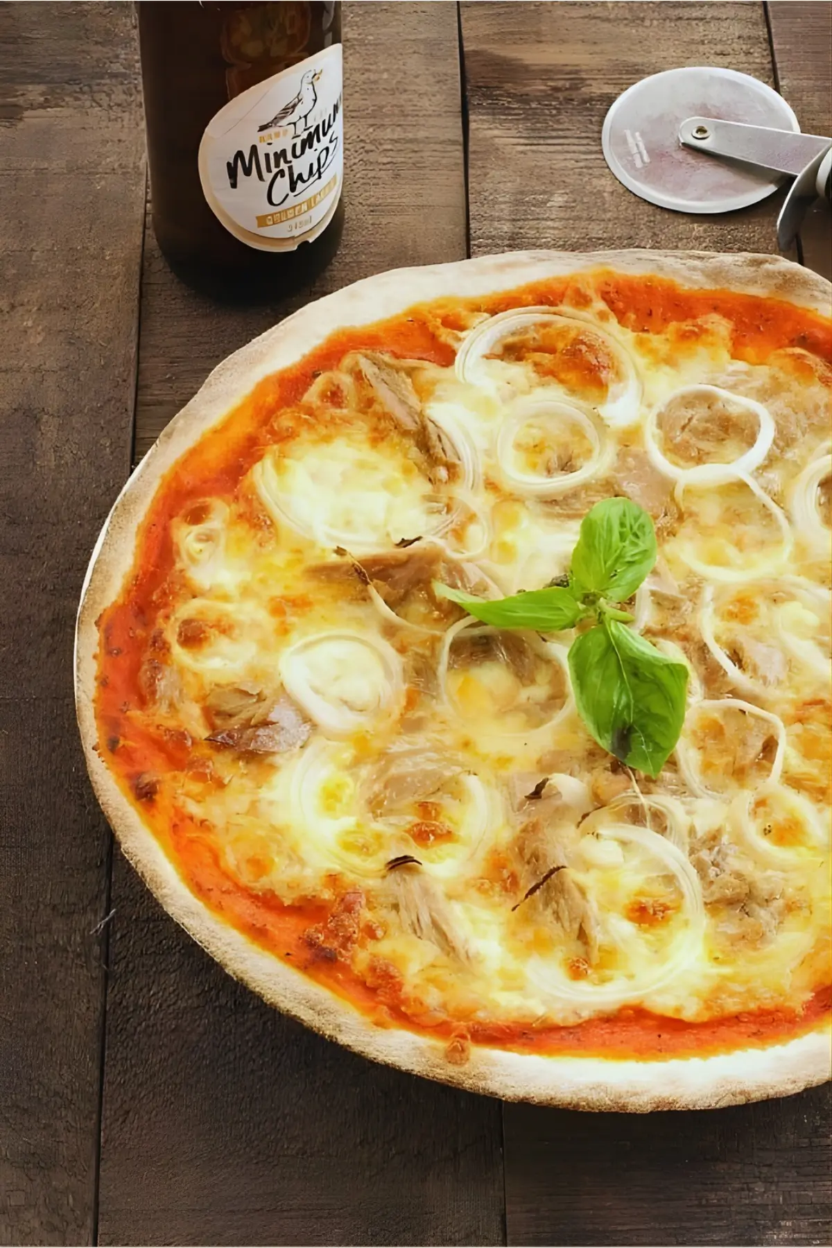 Baked tuna and onion pizza with melted cheese and basil on a wooden table.