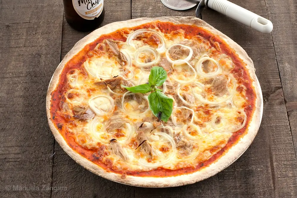 Top view of a tuna and onion pizza with melted cheese and fresh basil.