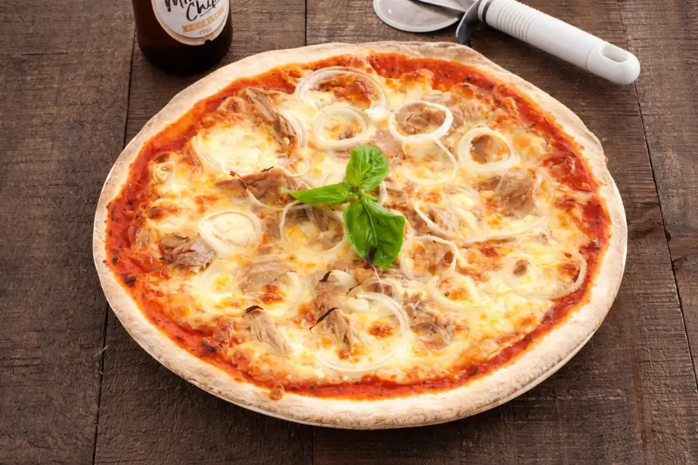 Golden tuna pizza fresh from the oven with bubbling cheese, onion slices, and basil on top.