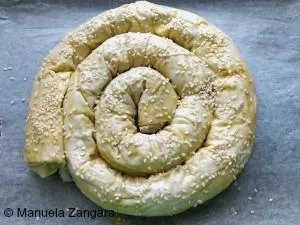 Unbaked burek spiral made with filo pastry, brushed with egg wash and sprinkled with sesame seeds.