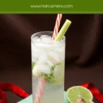 Tall glass cocktail with lime wedges, mint leaves, ice cubes, and a lemongrass stalk garnish.