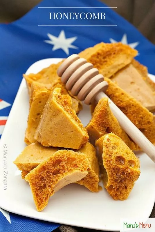 Pieces of golden honeycomb candy served with a honey dipper on a plate.