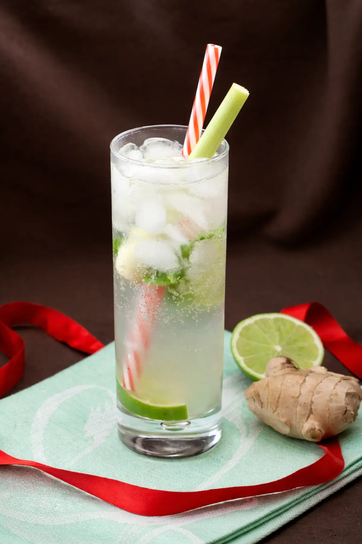 Chilled rum cocktail with lime slices, mint, ice cubes, and a fresh lemongrass stalk served beside ginger root and a halved lime.