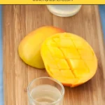 Chilled glass of mango liqueur beside ripe mango halves on a wooden board.