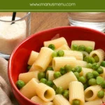 Close-up of short tube pasta with tender green peas in a red serving bowl.