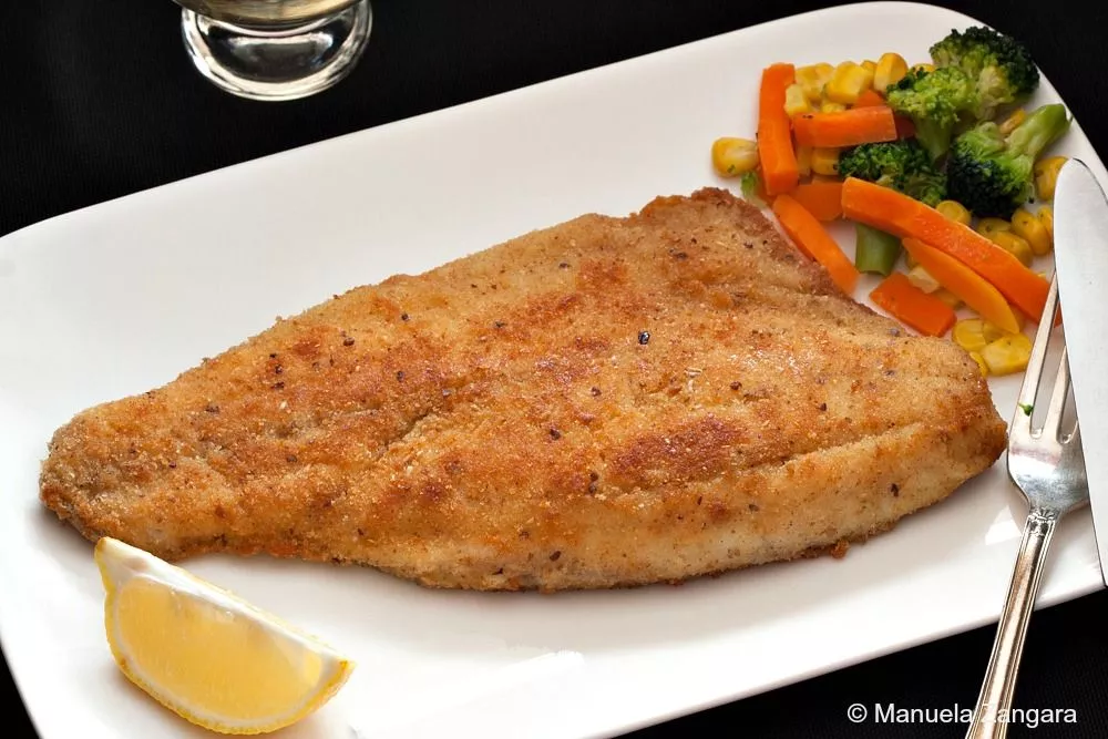 A plated serving of Crumbed Barramundi with vegetables and a lemon wedge.