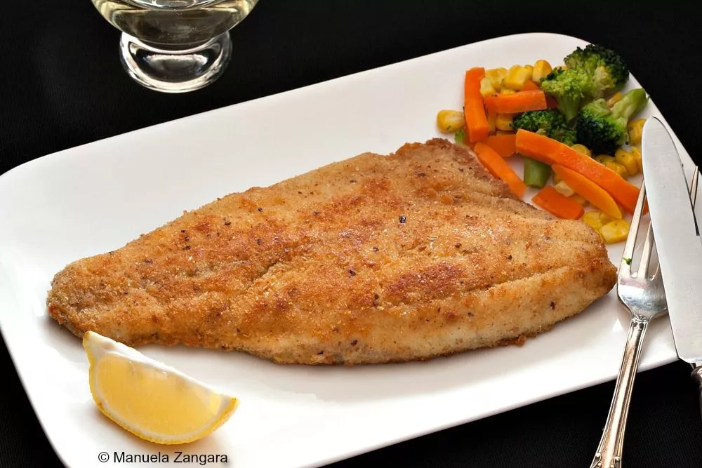 Crumbed Barramundi served with a side of mixed vegetables and a lemon wedge on a white plate.