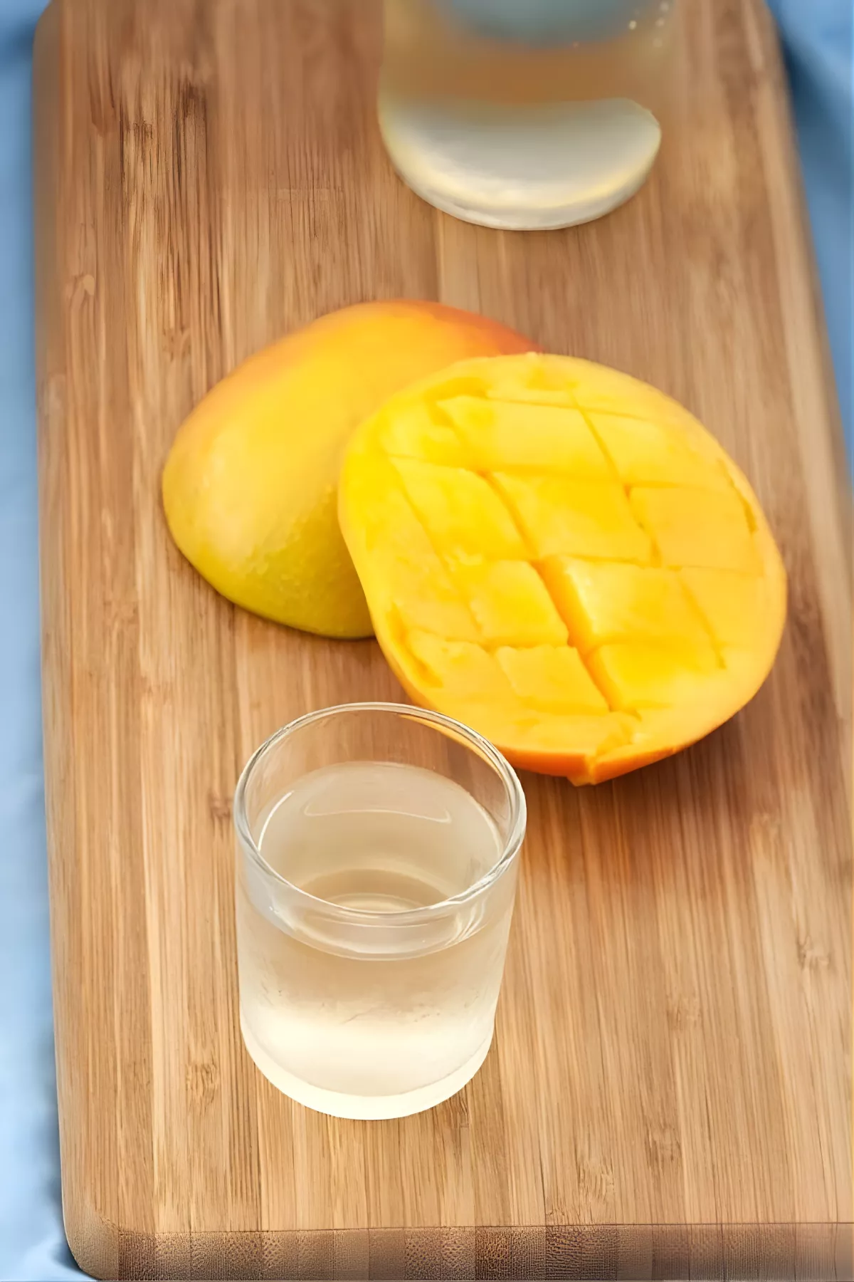 A glass of chilled liqueur with sliced mango on a wooden board.