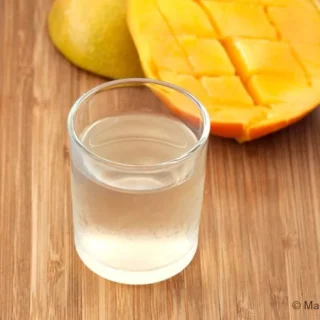 Chilled glass of mango liqueur beside ripe mango halves on a wooden board.