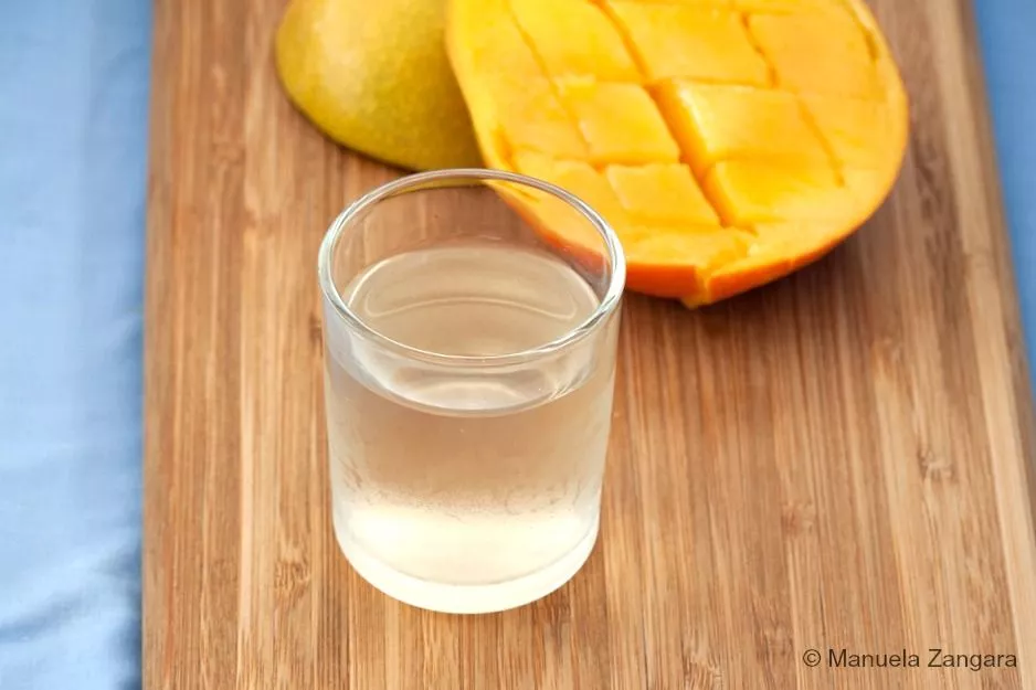 Chilled glass of mango liqueur beside ripe mango halves on a wooden board.