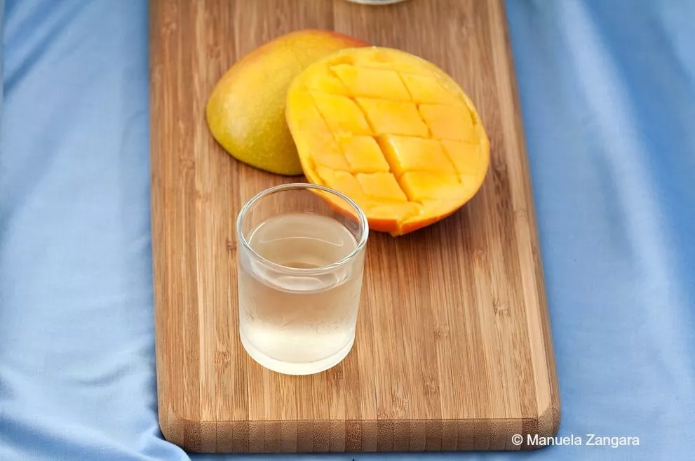 Close-up of a glass of Italian mango liqueur with fresh mango in the background.