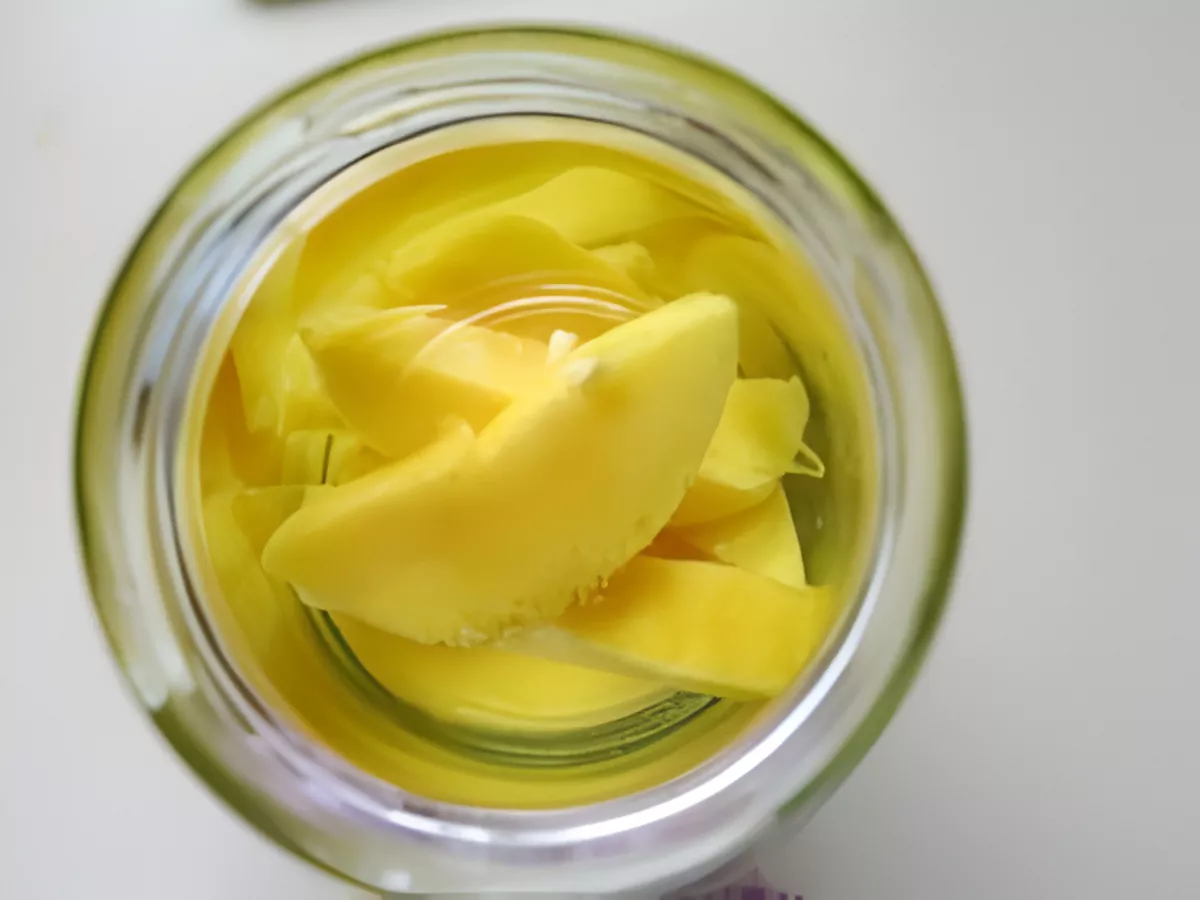 Fresh mango slices steeping in alcohol inside a glass jar to make homemade mango liqueur.
