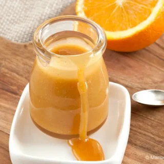 Close-up of orange caramel sauce dripping down a small glass jar on a white dish.