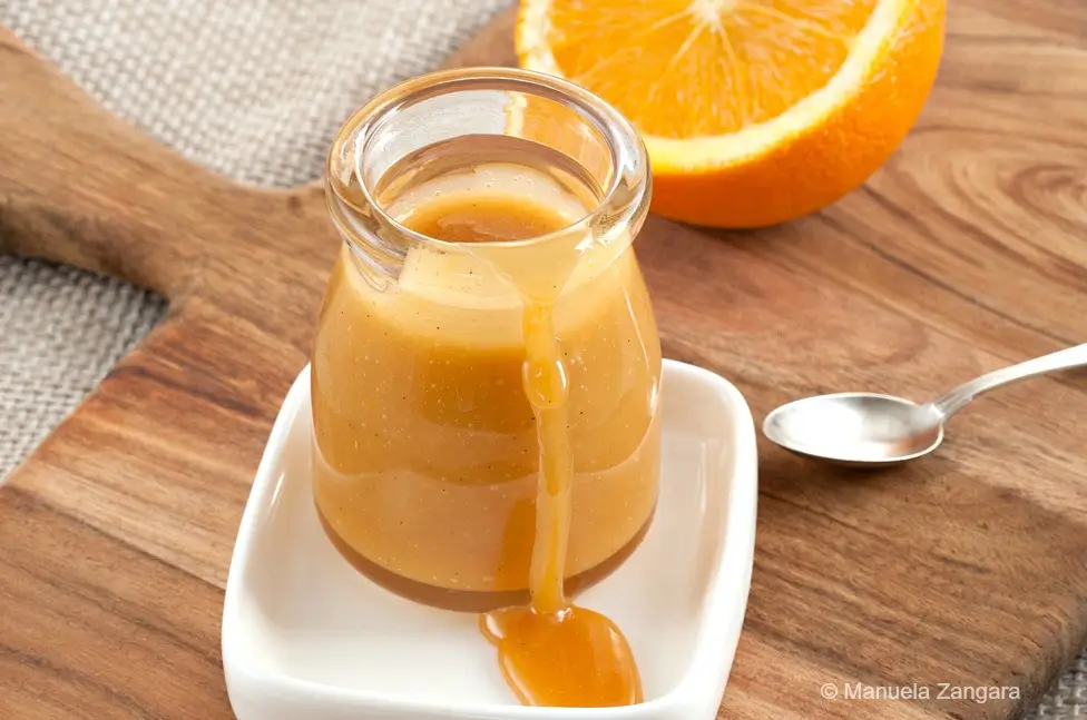 Close-up of orange caramel sauce dripping down a small glass jar on a white dish.