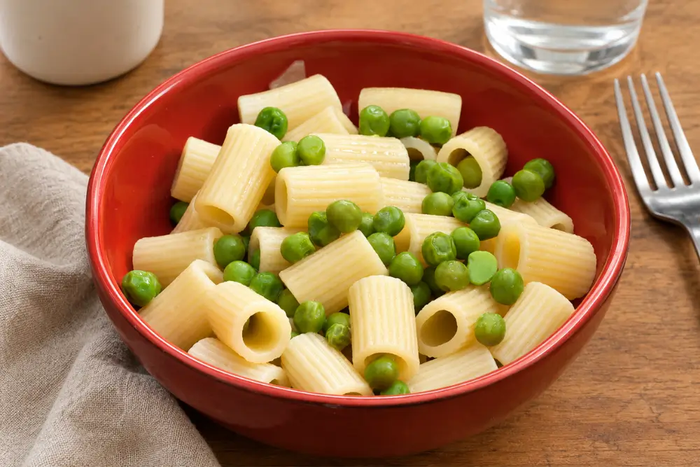 Pasta with Peas served in a red bowl with grated Pecorino Romano on the side.