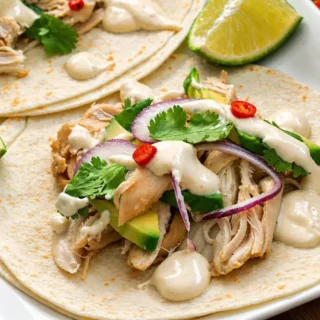 Chicken tacos with lime sour cream dressing, topped with avocado, red onion, and coriander.