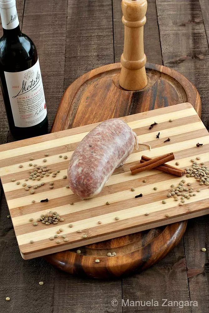 Homemade Cotechino on a wooden board with wine, cinnamon sticks, and lentils.