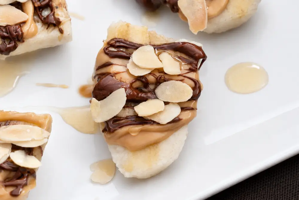 Close-up of a peanut butter banana bite with Nutella, honey, and toasted almond slices.