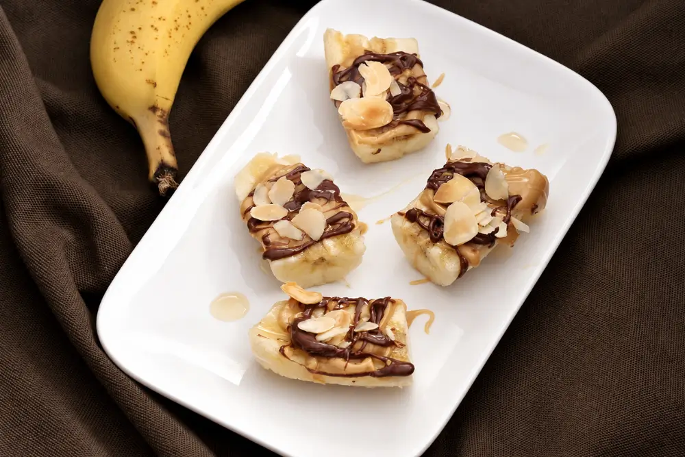 Peanut Butter Nutella Banana Bites topped with honey and toasted almonds on a white plate.