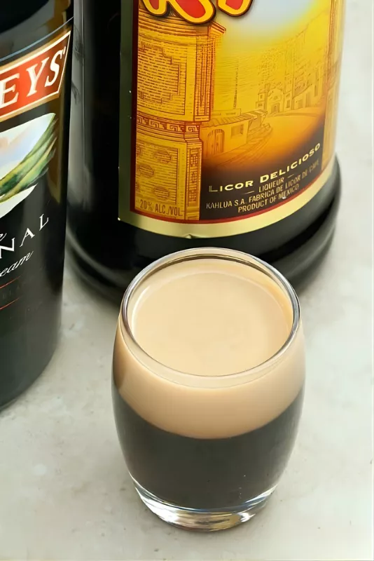 Baby Guinness layered shot with Baileys and Kahlua bottles in the background.