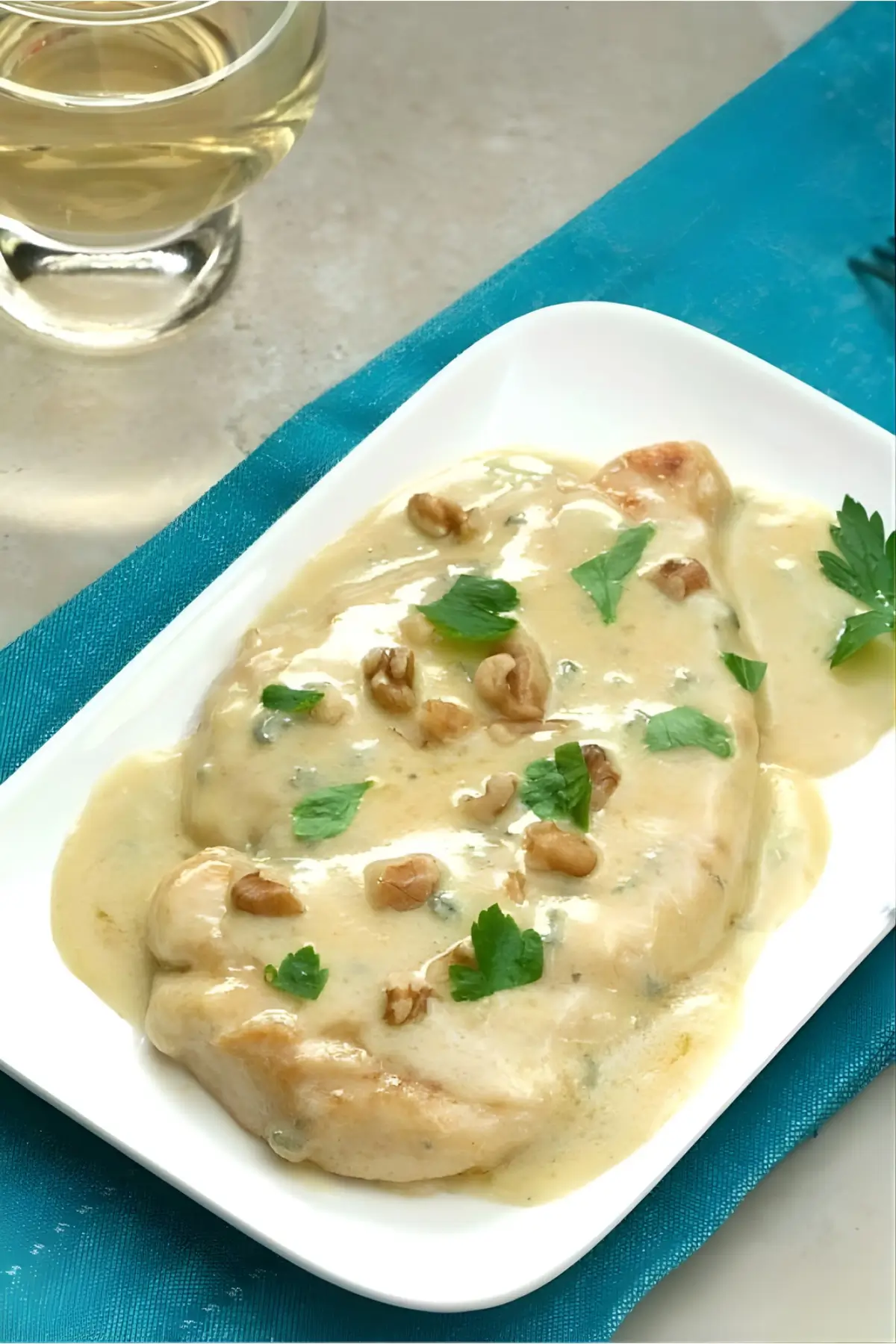 Chicken Gorgonzola plated with creamy sauce and herbs beside a glass of wine.