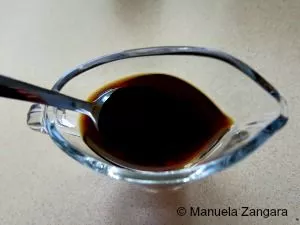 Ponzu sauce in a glass bowl with a spoon on a light surface.