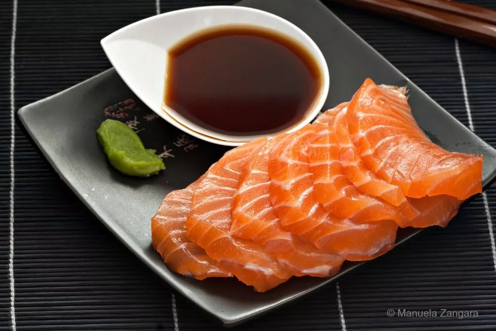 Salmon sashimi with Ponzu sauce and a small wasabi portion on a plate.