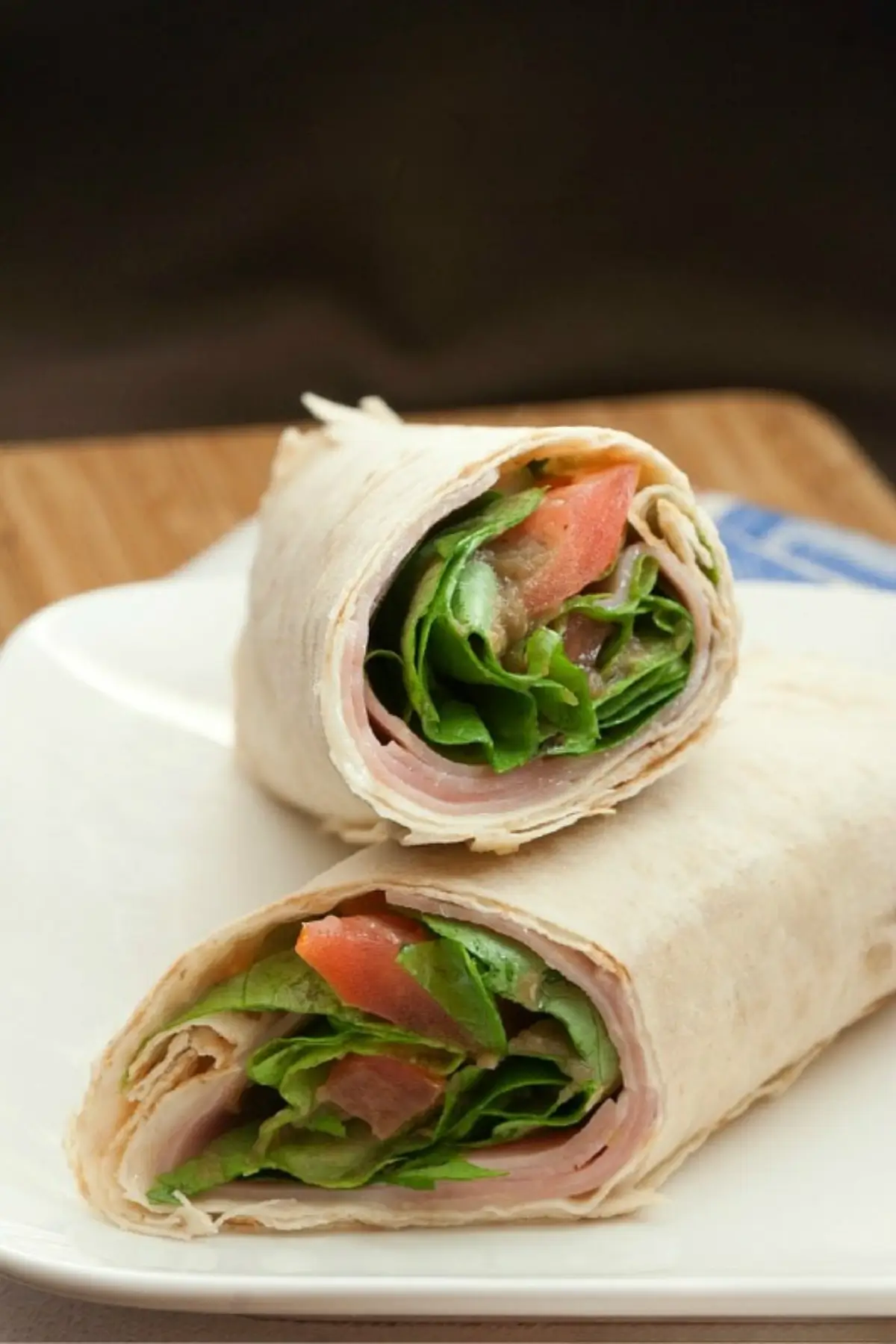 Close-up of a sliced ham wrap showing layers of lettuce, tomato, and thin ham inside.