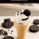 Cookies and Cream Frozen Yogurt served in a waffle cone with Oreo cookies on a marble countertop.
