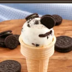 Scoop of cookies and cream frozen yogurt in a cone topped with Oreo pieces.