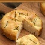 Golden baked Schiacciata topped with rosemary on a wooden board.