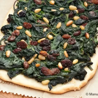 Close-up of baked coca topped with spinach, raisins, and pine nuts.