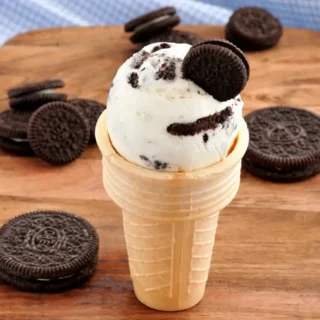 Scoop of cookies and cream frozen yogurt in a cone topped with Oreo pieces.