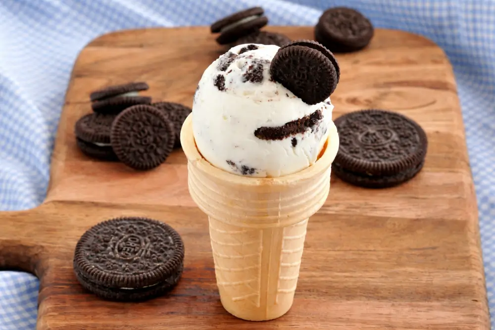 Scoop of cookies and cream frozen yogurt in a cone topped with Oreo pieces.