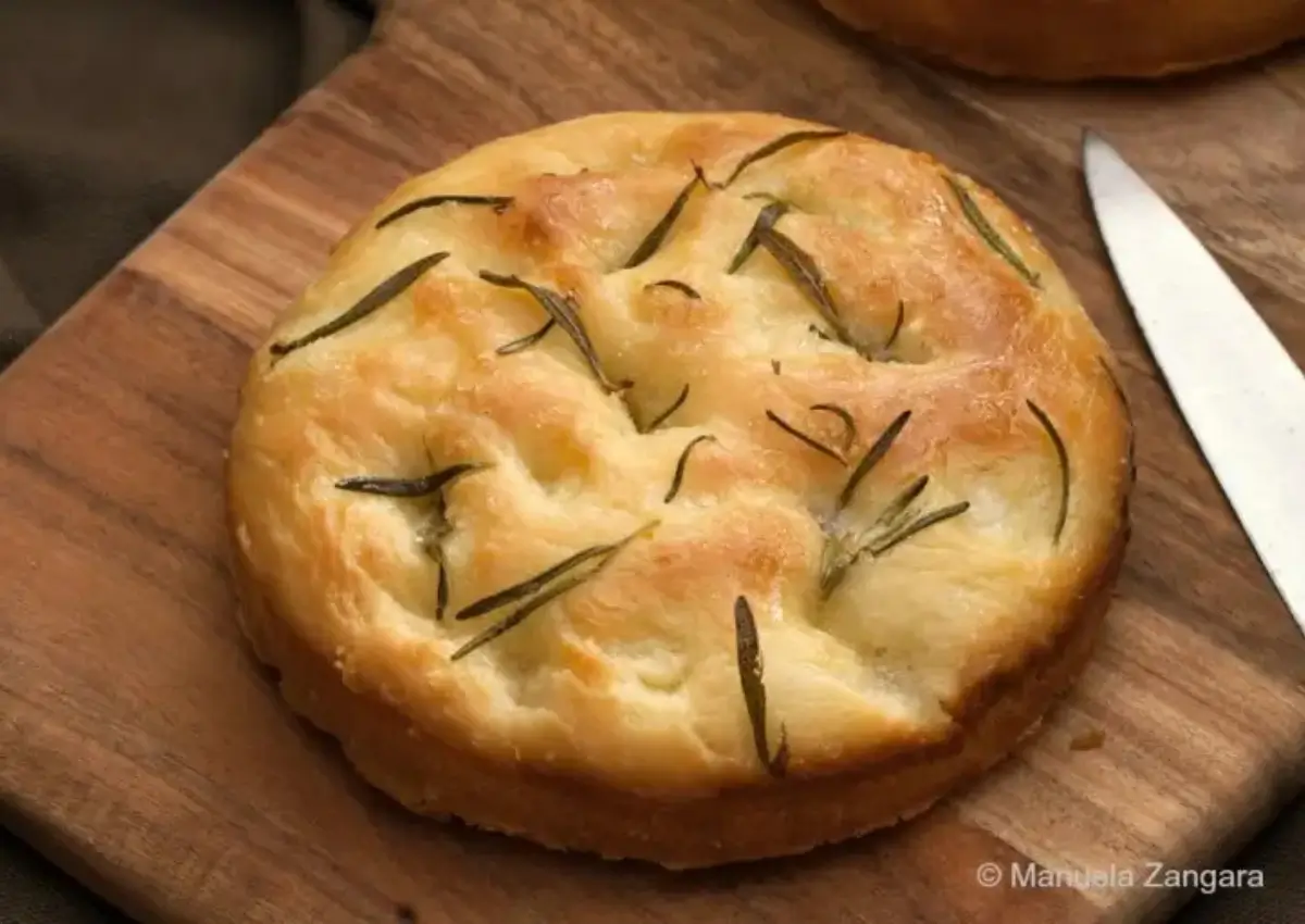 Golden baked Schiacciata topped with rosemary on a wooden board.