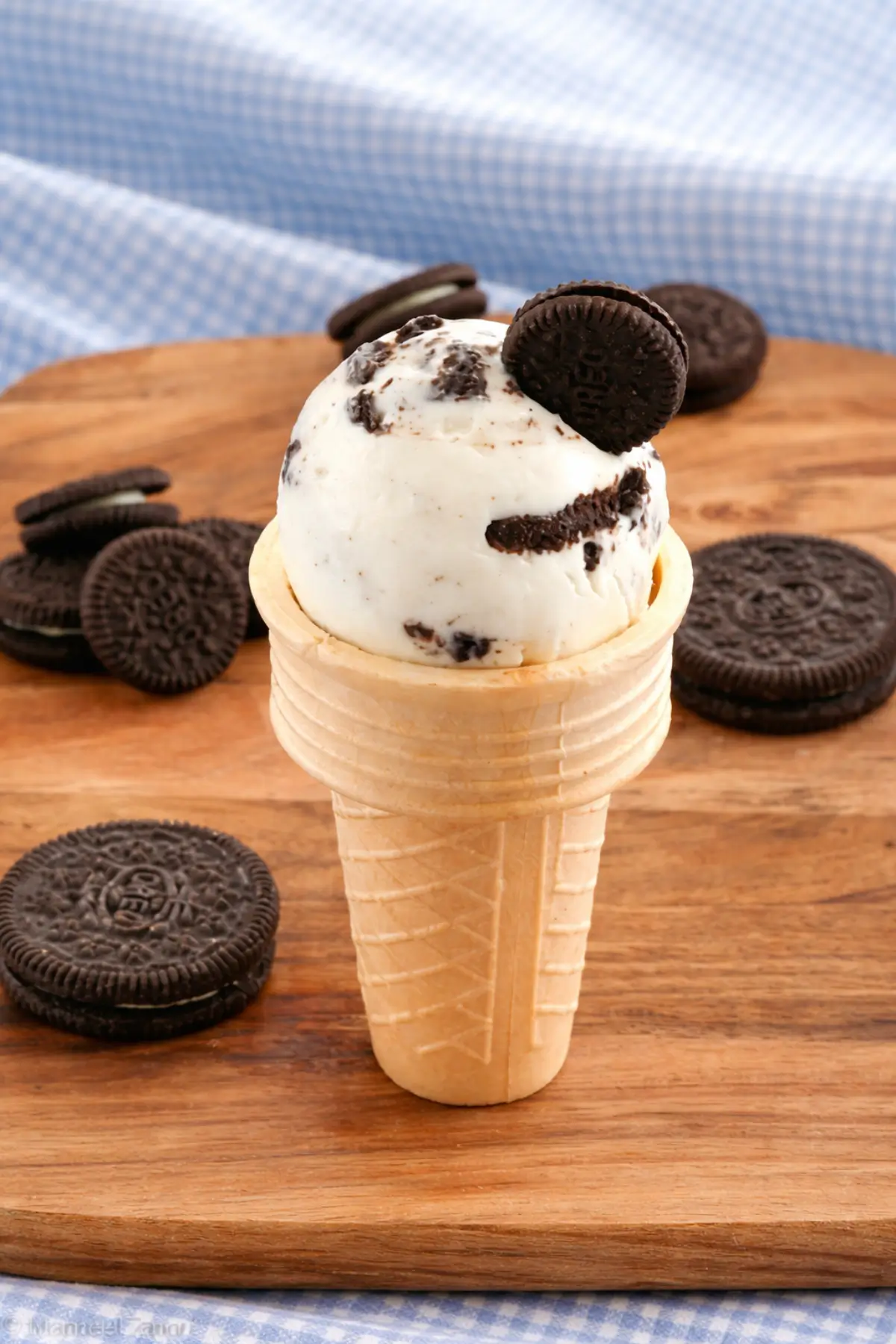 Creamy frozen yogurt with chocolate biscuit pieces served in a waffle cone on a wooden board.