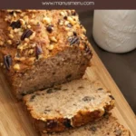 Copycat Starbucks Banana Nut Bread topped with chopped walnuts and pecans beside a milk jar on a wooden board.
