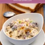 Close-up of chicken salad with chunks of chicken, grapes, and chopped onions coated in a thick dressing.