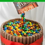 Finished M&M’s Kit Kat cake with a red ribbon and a floating candy effect.