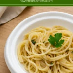 Pasta with Garlic and Parsley served in a white ceramic bowl on a light oak tabletop.