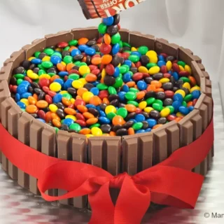 Finished M&M’s Kit Kat cake with a red ribbon and a floating candy effect.