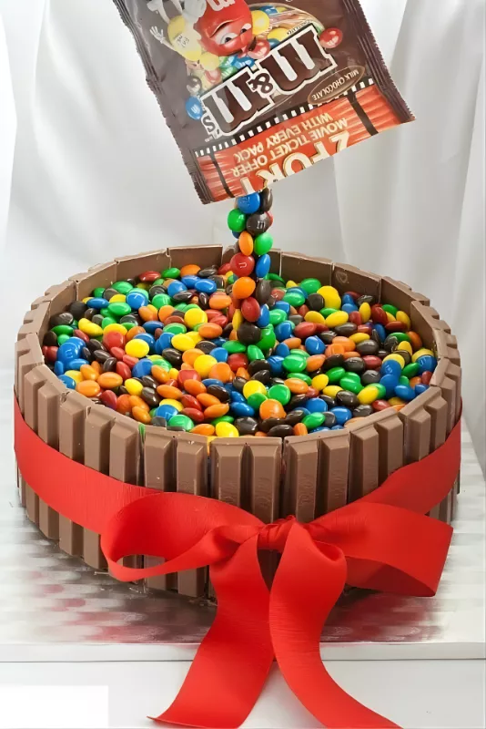 Gravity-defying M&M’s Kit Kat cake decorated with a red ribbon and colorful candies.