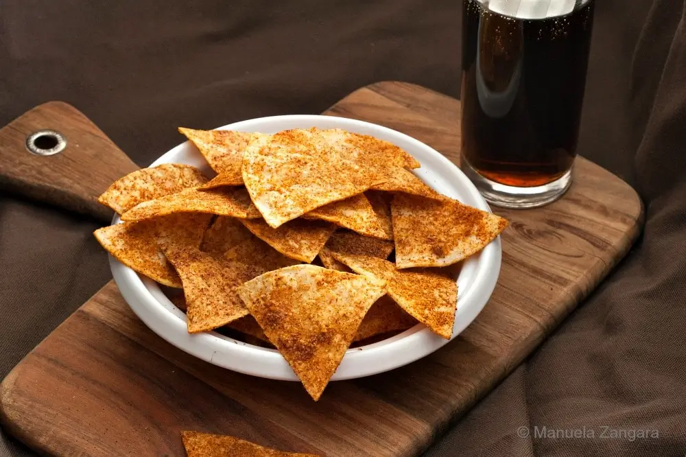 Close-up top view of baked homemade Doritos piled in a white bowl.